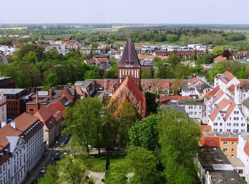 Das Bild zeigt eine Luftaufnahme der Greifswalder St. Marien Kirche mit umliegenden Wohngebäuden und Bäumen.