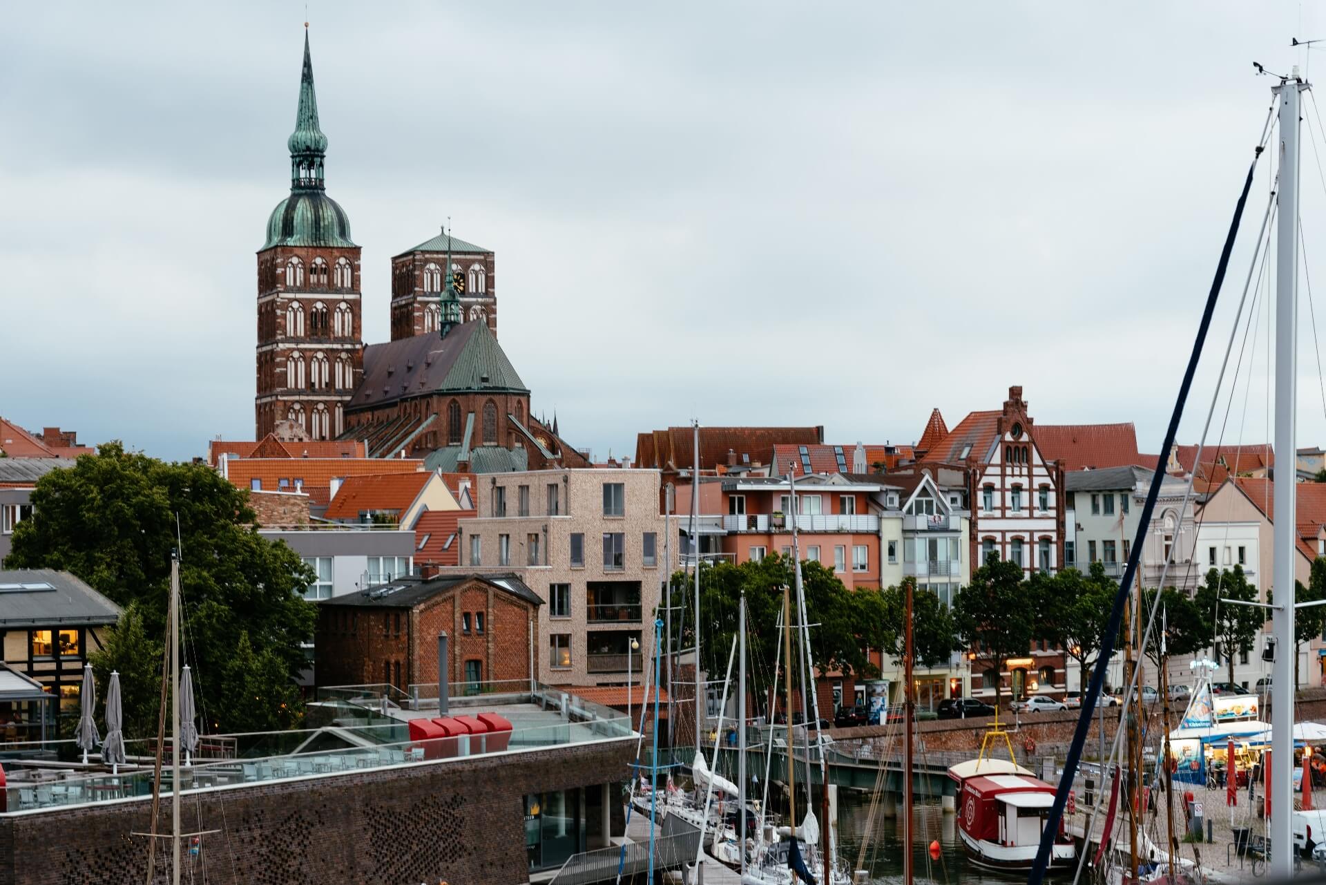 Das Bild zeigt im Vordergrund den Stralsunder Hafen mit Segelbooten und im Hintergrund die St. Nikolai Kirche.